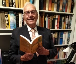 Emil Gätjens vor seinem Bücherregal, mit dem Buch „Arme und Reiche